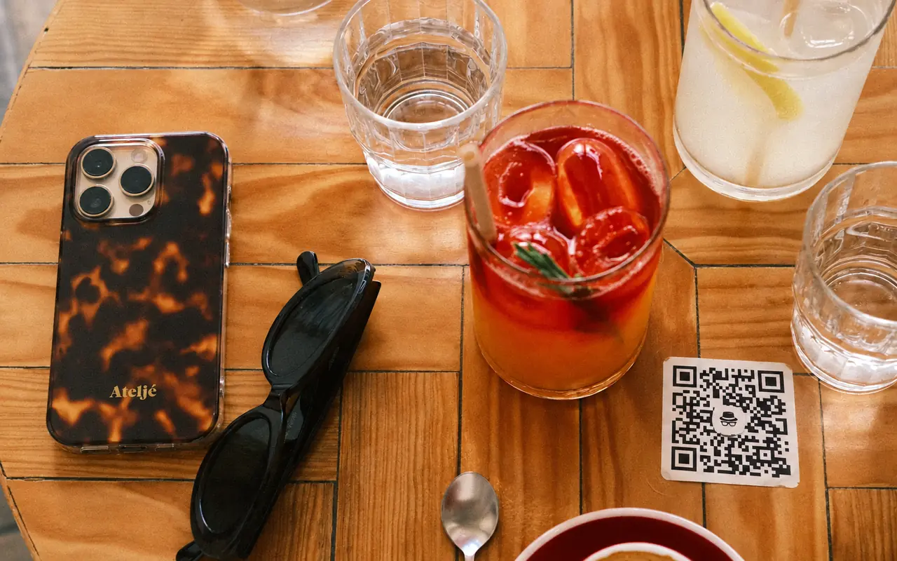 Cod QR cu sigla WebHat aplicat pe o masă de cafenea, lângă telefon și băuturi