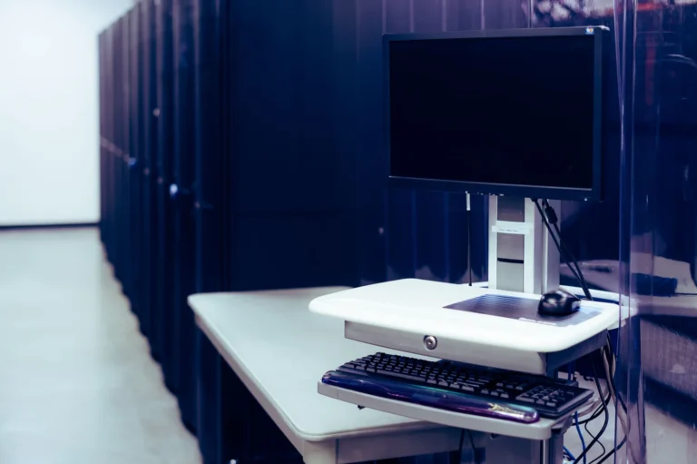 Monitor și tastatură pe o stație de lucru lângă rackuri de servere
