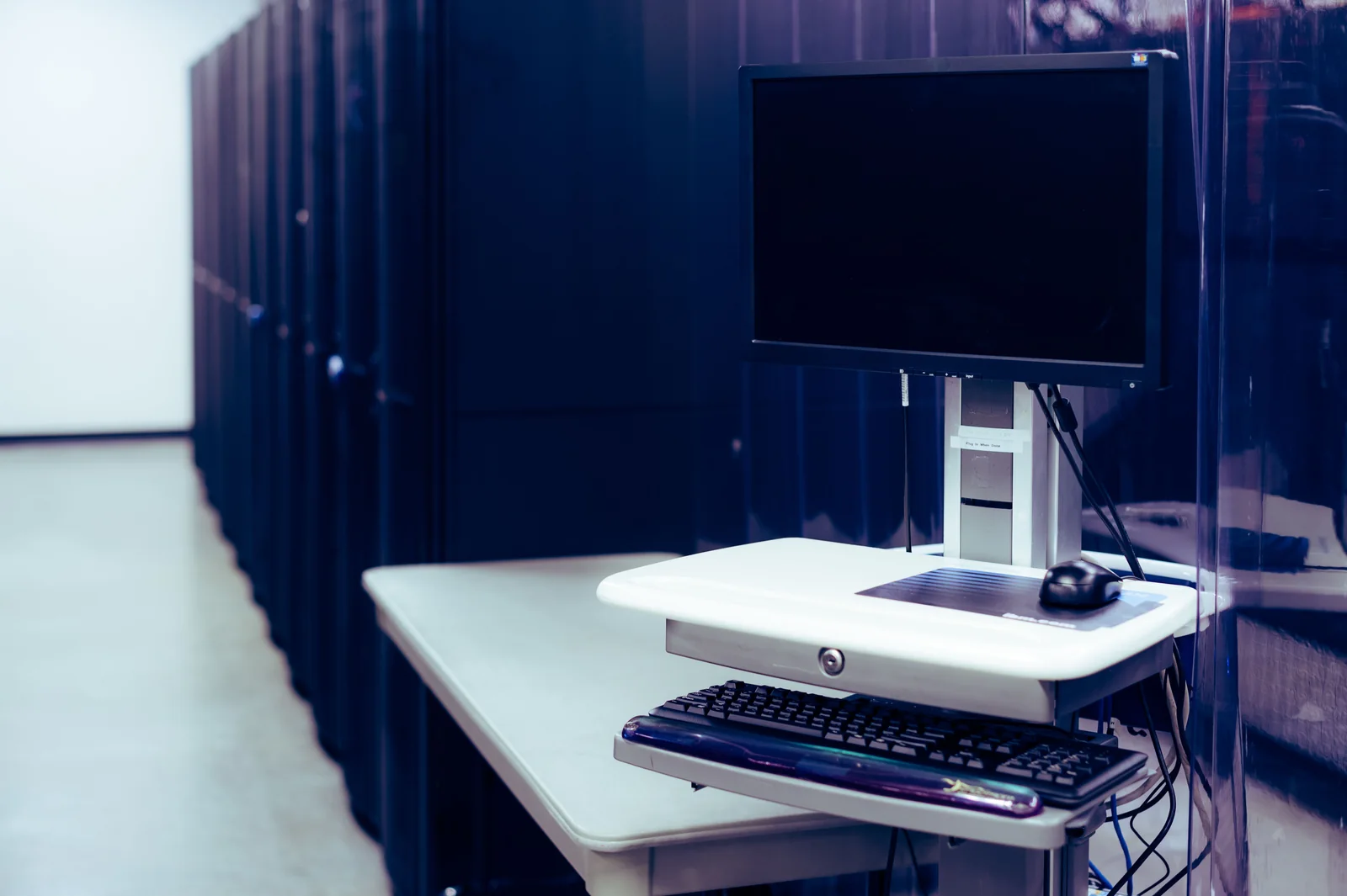 Monitor și tastatură pe o stație de lucru lângă rackuri de servere