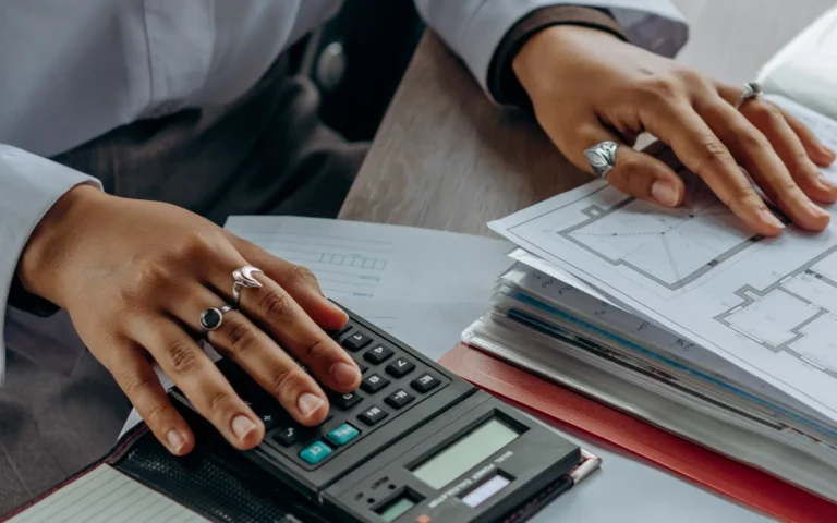 Mâini folosind un calculator lângă un teanc de documente